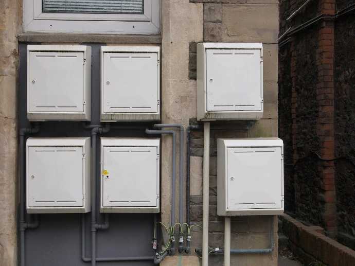 Five white utility boxes mounted on a stone and grey wall with pipes